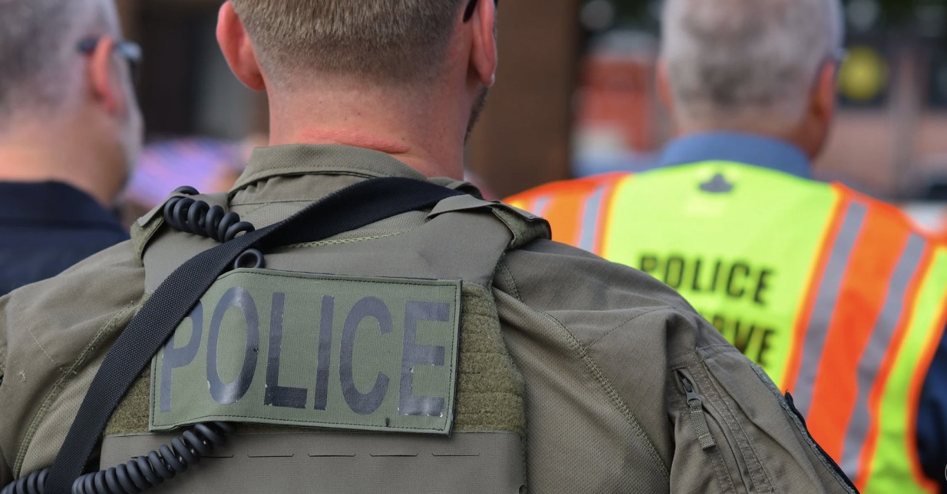 Police officer in tactical vest viewed from behind — no face shown